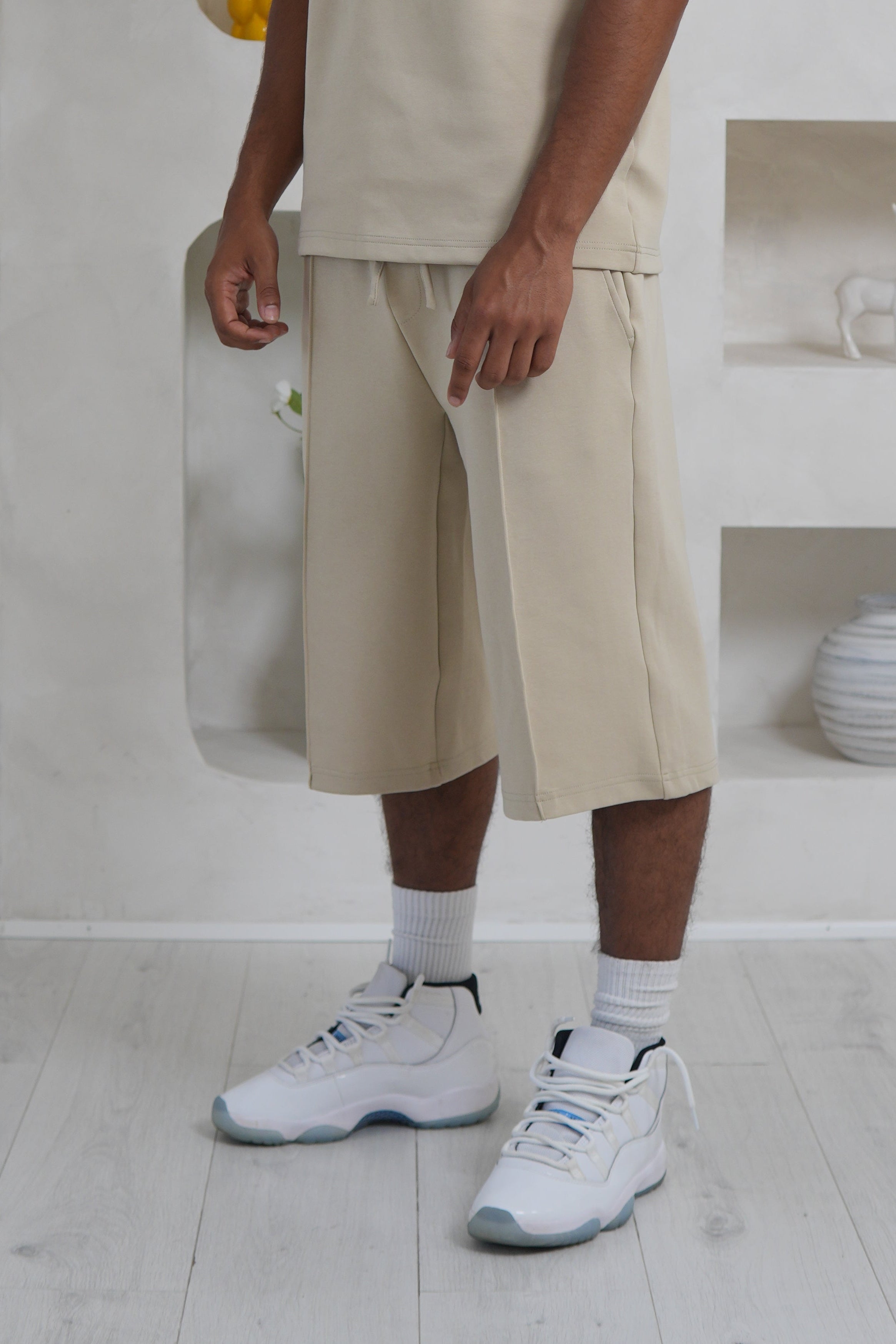 Man wearing a beige outfit standing in a minimalistic room with white walls and light-colored flooring. YAZIR