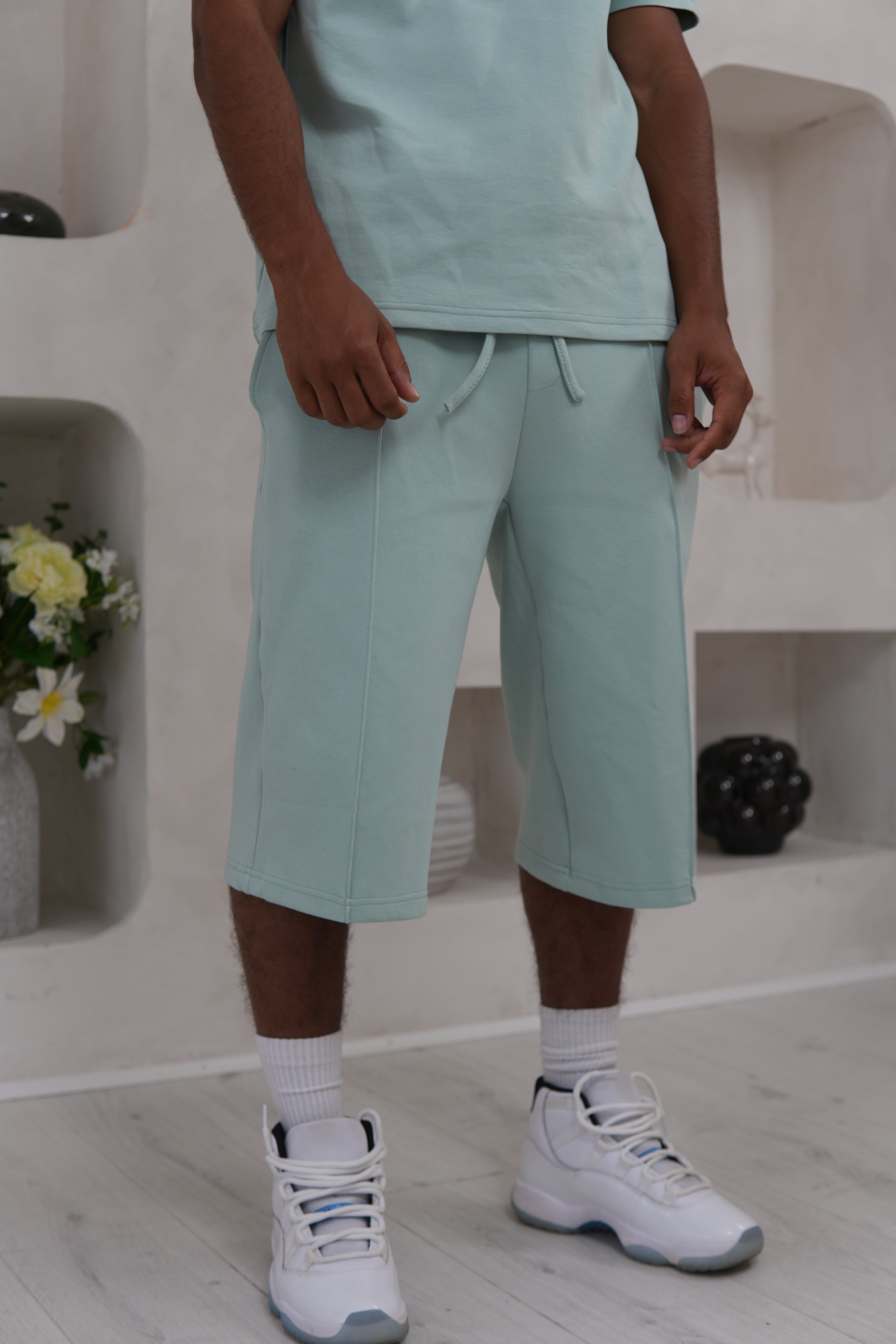 Person wearing sage green pants and white sneakers in a minimal indoor setting.