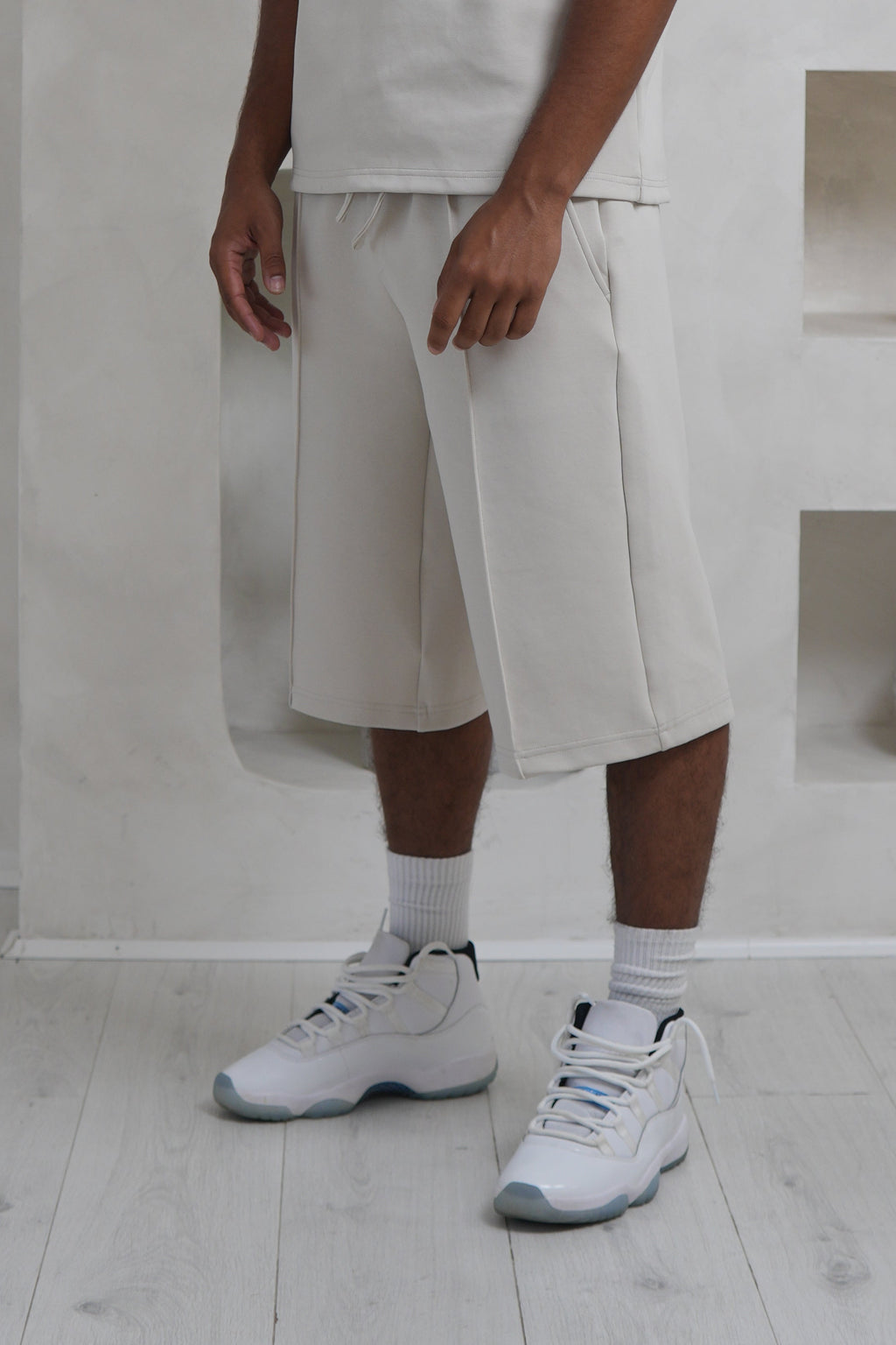 Person wearing a white outfit standing in a minimalistic room with white walls and floor.