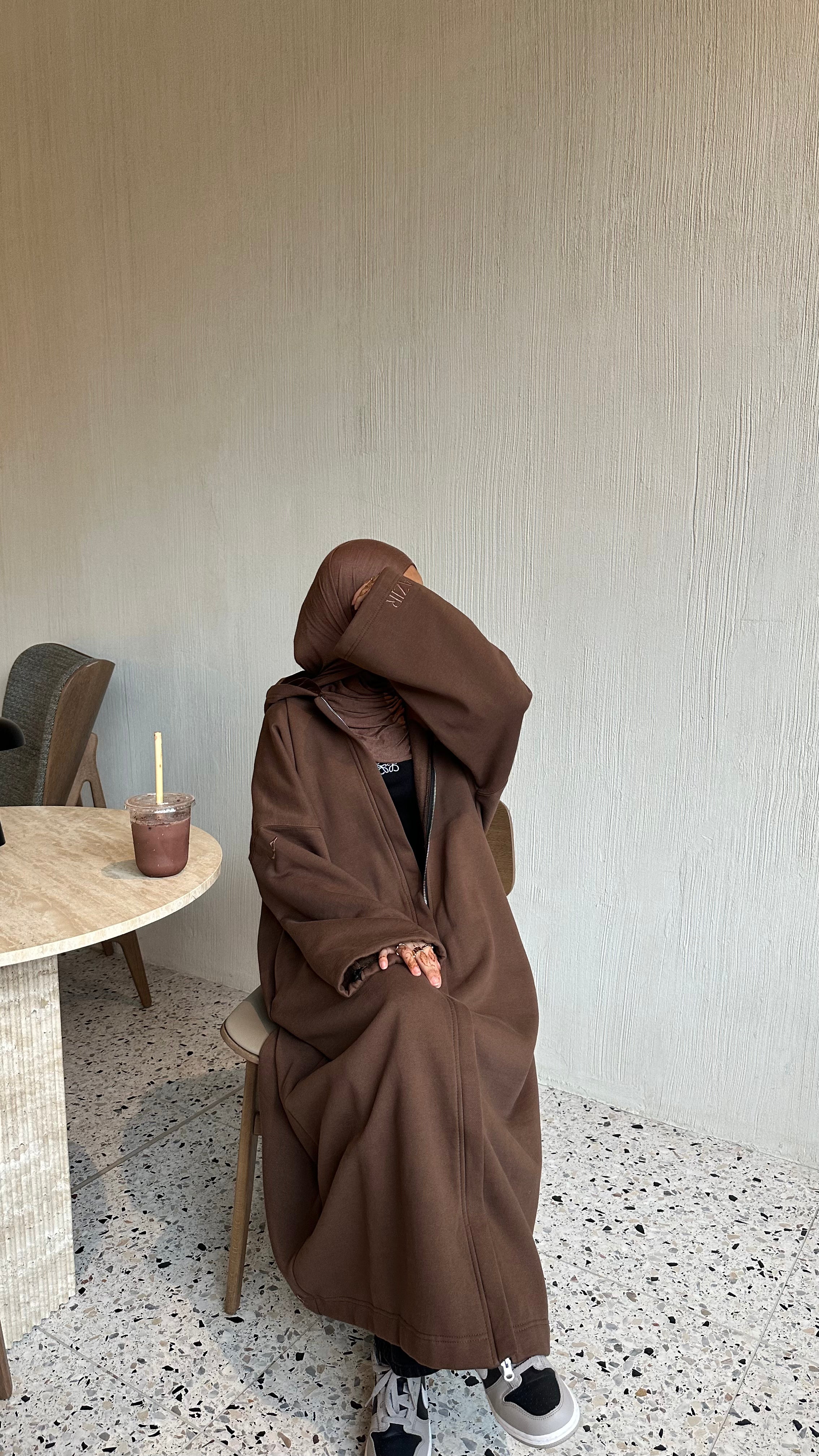 A long coat winter abaya, brown coloured, designed to keep you warm in the winter with a hoodie and a zip. Oversized size with strings on the hands to become cuffed.